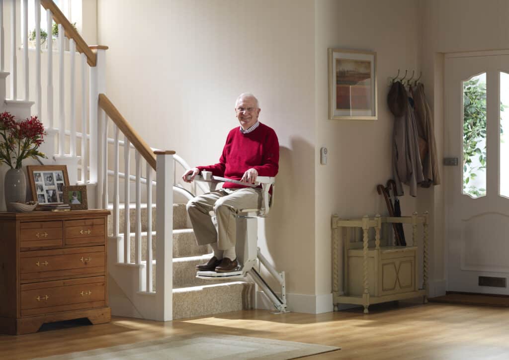 Man on a stairlift moving along a curved rail at the bottom of a staircase.