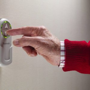 Close up of an older person's hand pressing an arrow button on a wall mounted remote control unit.