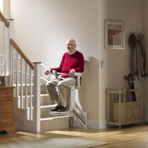 Man on a stairlift moving along a curved rail at the bottom of a staircase.