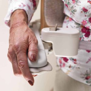 A close up view of a woman's hand using the grey toggle control located on the armrest of a stairlift.